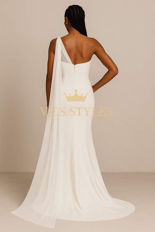 Woman wearing a white one-shoulder gown with a cape, standing against a beige background.– V.E.S. Styles