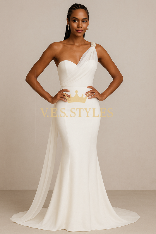 Woman wearing a white one-shoulder gown with a crown detail, standing against a beige background. – V.E.S. Styles
